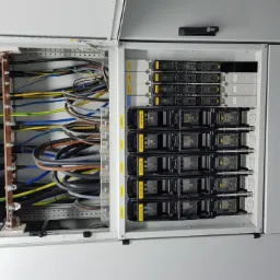 Otwarta szafa elektryczna z widocznymi przewodami, szynami zbiorczymi z miedzianymi elementami i zabezpieczeniami modułowymi, zamontowana w pomieszczeniu technicznym.