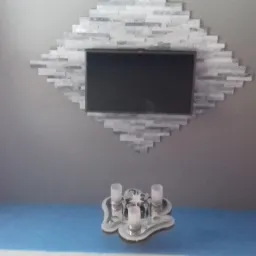 Telewizor zawieszony na szarej ścianie z dekoracyjną ramą z szarej mozaiki, pod nim dekoracyjny świecznik na niebieskiej podłodze, ściany pomalowane na różowo i szaro.