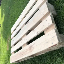 Świeżo zbita, jasna paleta drewniana leżąca na zielonej trawie, widoczne sęki i gwoździe.