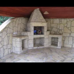 Kamienny grill ogrodowy z wnękami na drewno, wykończony nieregularnymi płytami piaskowca, z drewnianym zadaszeniem i wiszącą lampą.