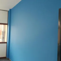 Świeżo pomalowana ściana na jasny odcień błękitu w pokoju z białym sufitem i płytkami podłogowymi, widoczna futryna okienna i fragment czarnych drzwi.