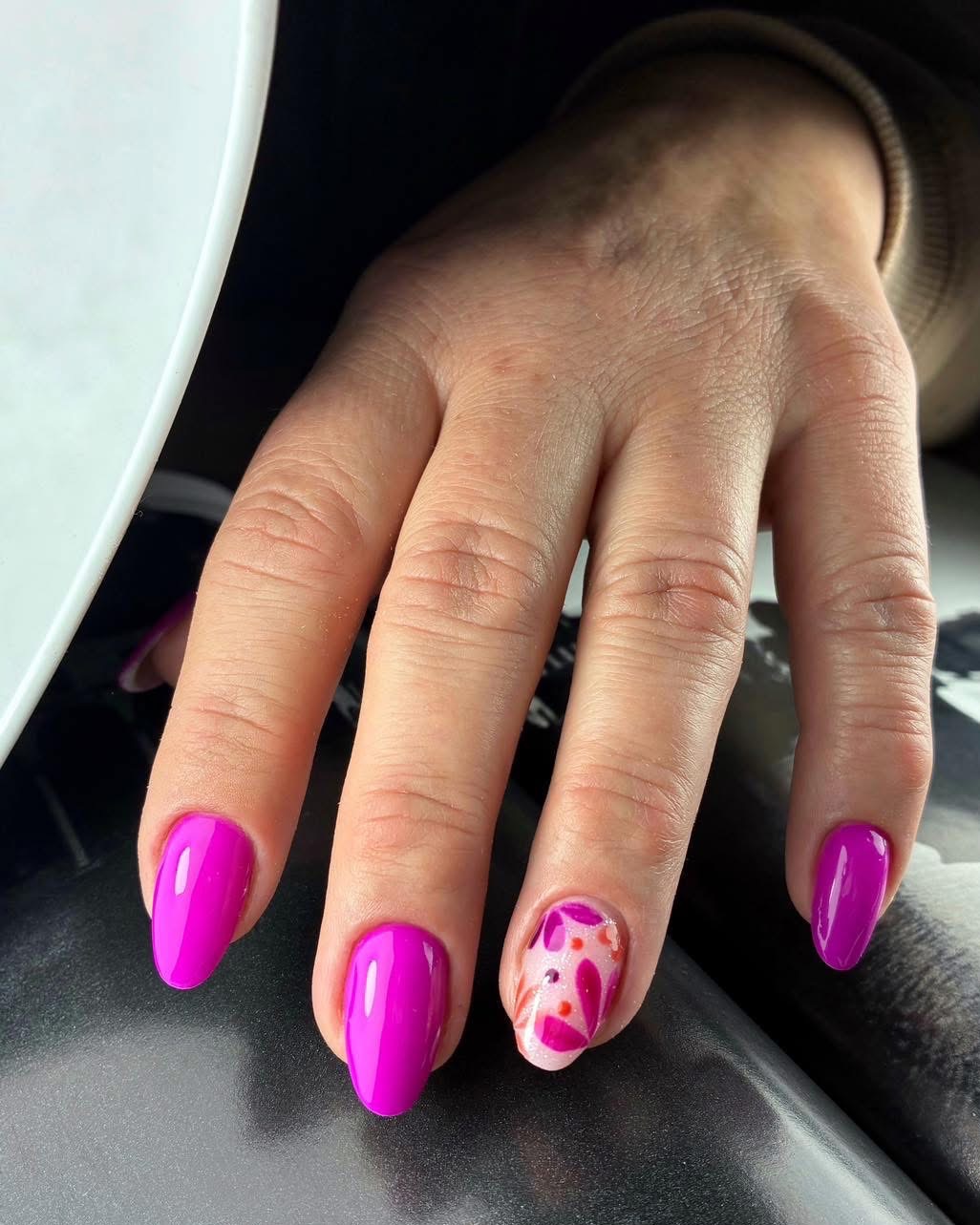 Dłoń z fuksjowymi paznokciami, jeden z wzorem kwiatowym. Błyszczący manicure hybrydowy w odcieniach różu i bieli, wykonany w salonie kosmetycznym.