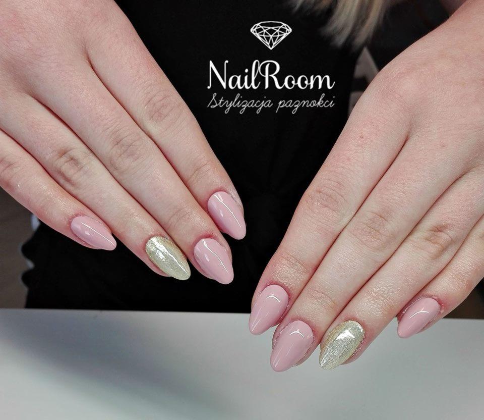 Dłonie z świeżo pomalowanymi paznokciami w odcieniach pudrowego różu i złota, kształt migdał, widoczne logo salonu stylizacji paznokci w tle.