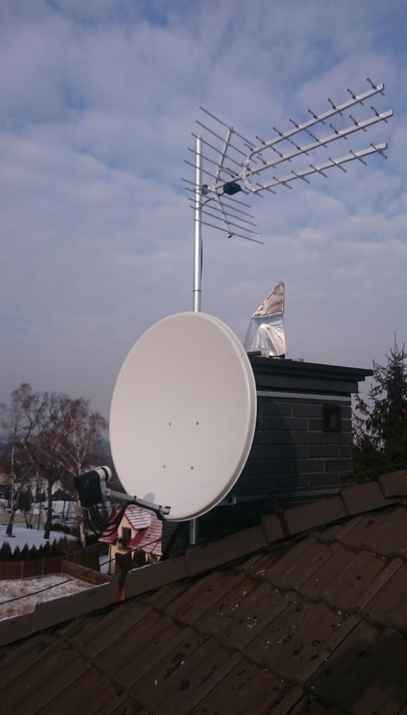 Antena satelitarna i antena naziemna zamontowane na dachu budynku z kominem, widok na zimowy krajobraz.