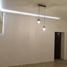 Wykończona kawalerka w Darłowie: białe ściany, panelowa podłoga, nowoczesne oświetlenie sufitowe LED i dwie lampy wiszące w stylu industrialnym.