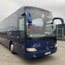 Kempny Transport - Niebieski autokar marki Mercedes-Benz Tourismo z logo firmy Kempny Transport, zaparkowany na chodniku z kostki brukowej. Widok z przodu i z boku, tablica rejestracyjna SPS 86216.