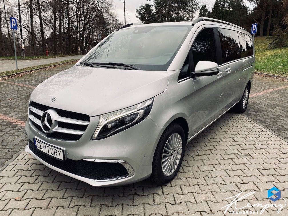 Srebrny Mercedes-Benz V-klasy na parkingu z kostki, znak drogowy P w tle. Auto z relingami dachowymi i przyciemnianymi szybami.
