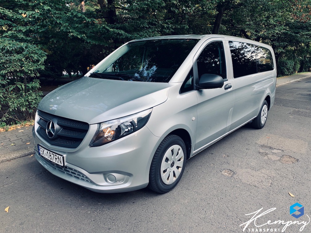 Srebrny Mercedes Vito z widoczną tablicą rejestracyjną SK 187RN, zaparkowany na ulicy z zielonym tłem drzew. Logo firmy transportowej w prawym dolnym rogu.
