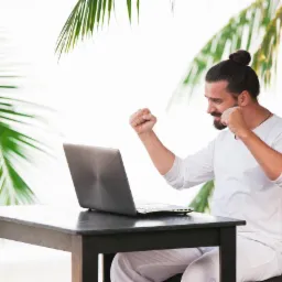 Mężczyzna w białym ubraniu siedzi przy ciemnym drewnianym stole z laptopem, zaciśniętymi pięściami w geście triumfu, na tle tropikalnej roślinności.