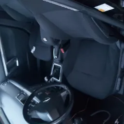 Wnętrze samochodu z widocznymi czarnymi fotelami, kierownicą i elementami deski rozdzielczej, sfotografowane z nietypowej perspektywy z góry.