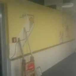 Ż&oacute;łta ściana w korytarzu z rysunkami, w trakcie malowania, widoczna drabina malarska i niedomalowany fragment ściany przy rysunku lod&oacute;w.