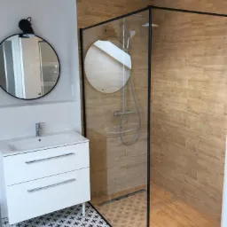 Nowoczesna łazienka z kabiną prysznicową typu walk-in z czarną ramą, umywalką z szafką na nóżkach, okrągłym lustrem z czarnym oświetleniem i wzorzystą podłogą.