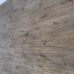 Ściana wykończona panelami imitującymi drewno, widoczne detale struktury drewna i połączenia między panelami, ujęcie z boku.