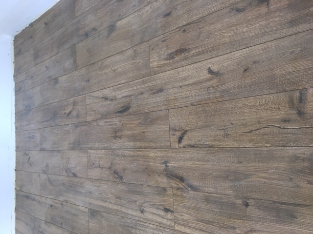 Ściana wykończona panelami imitującymi drewno, widoczne detale struktury drewna i połączenia między panelami, ujęcie z boku.