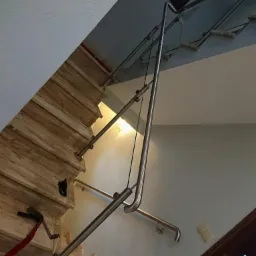 Wewnętrzne schody wyłożone marmurem, z nowoczesną balustradą ze stali nierdzewnej i szklanymi panelami, widziane z dołu pod kątem, z elementami dekoracyjnymi na ścianie w tle.