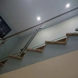 Szklana balustrada schodowa z nierdzewną poręczą, mocowana punktowo, widok z dołu, na ścianie obraz z motywem miejskim.