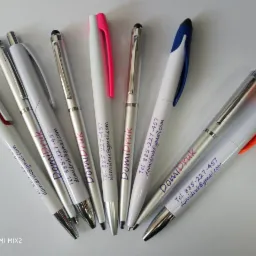 Zestaw długopisów reklamowych z nadrukiem 'DomiDruk' i danymi kontaktowymi firmy z Przylepu, widoczne różne kolory wstawek: czerwony, różowy, niebieski i pomarańczowy.