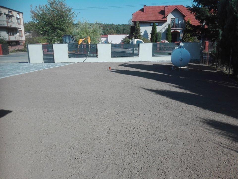 Przygotowany teren pod trawnik z widoczną ziemią ogrodową, ogrodzeniem panelowym i zbiornikiem na gaz w tle.
