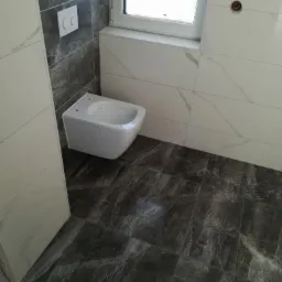 Nowoczesna łazienka z szarymi płytkami imitującymi marmur na podłodze i ścianach, wisząca toaleta oraz okno z białym parapetem.