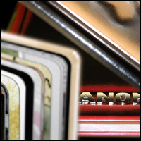 Stos fotoalbumów z zaokrąglonymi rogami, widoczne różne okładki i grzbiety, na jednym z albumów złoty napis.