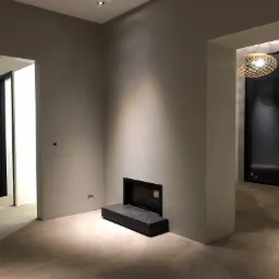 Wnętrze po pracach wykończeniowych: gładkie, szare ściany, wbudowany kominek z czarną obudową, trzy punktowe lampy sufitowe i ozdobna lampa wisząca w tle.