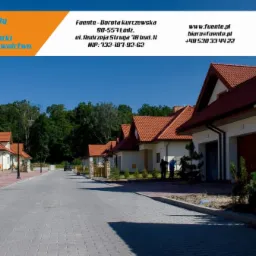 Ulica osiedlowa z kostki brukowej prowadząca do szeregu nowych domów jednorodzinnych z czerwonymi dachami; widoczny fragment logo firmy budowlanej w górnym rogu.