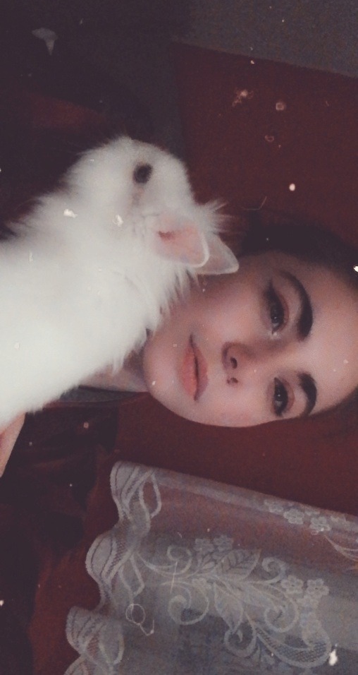 Portret młodej kobiety leżącej na bordowym tle z białym królikiem na ramieniu, widoczne fragmenty koronkowej narzuty