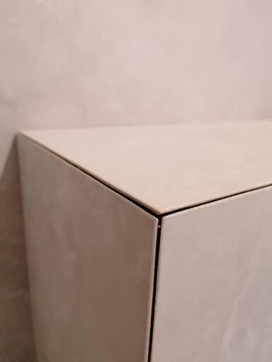 Detal wykończenia narożnika obudowy z płytek ceramicznych w łazience, z widoczną fugą i fakturą płytek.