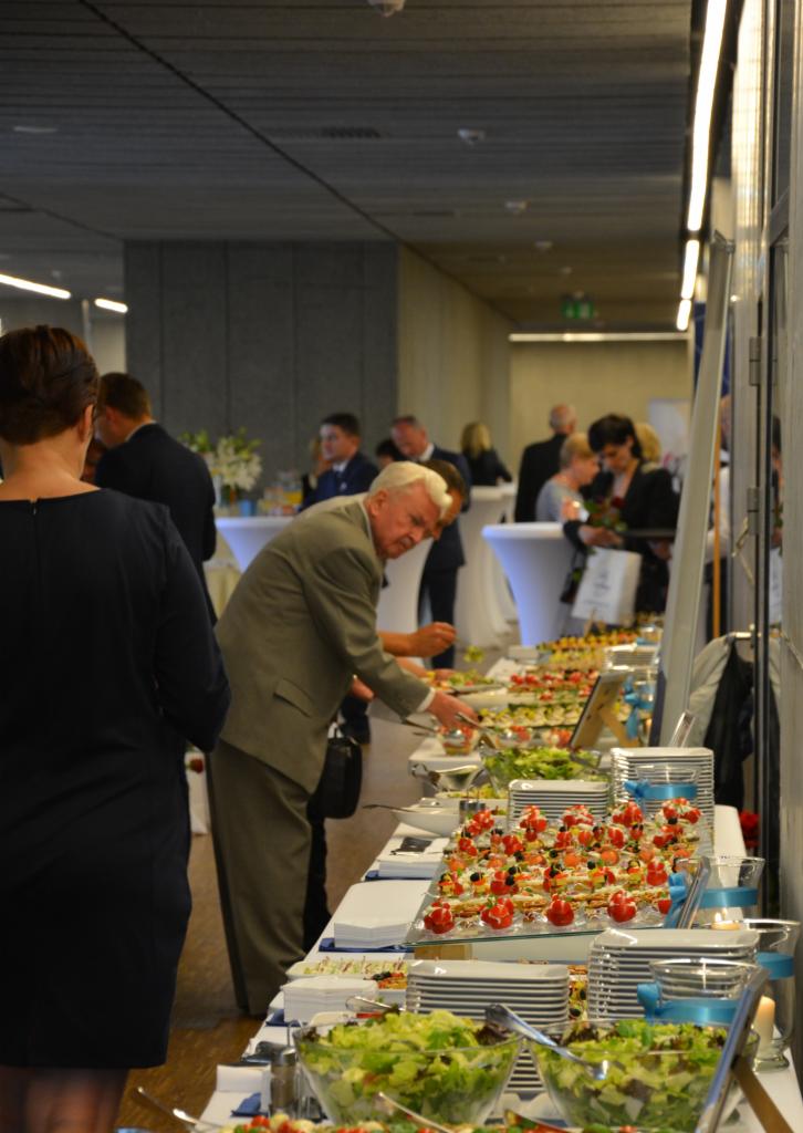 Bufet cateringowy z sałatkami, kanapeczkami i osobami w tle podczas wydarzenia firmowego.