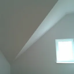 Poddasze po remoncie z oknem dachowym, świeżo pomalowane na biało, widoczne gładkie ściany i skosy.