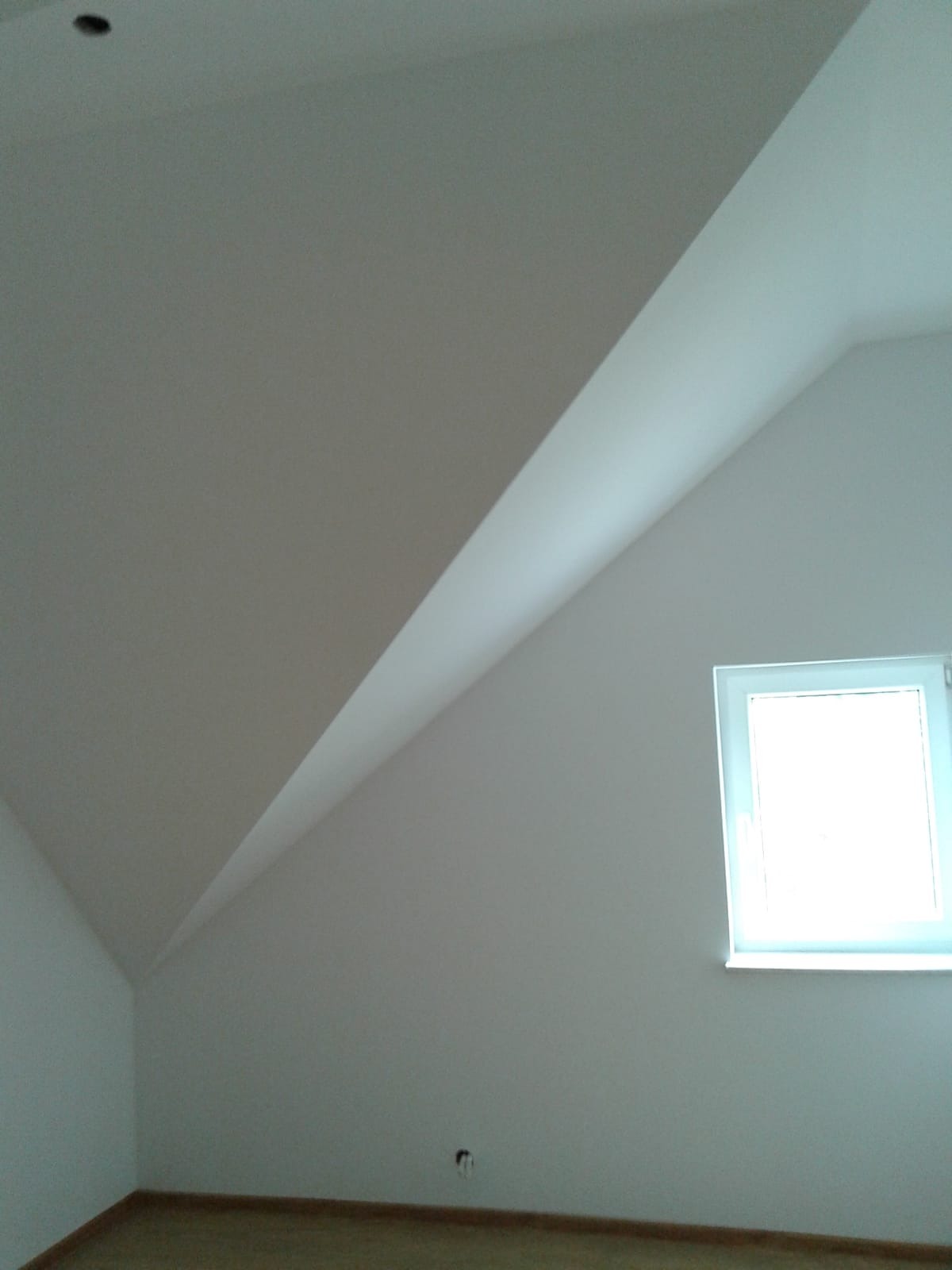 Poddasze po remoncie z oknem dachowym, świeżo pomalowane na biało, widoczne gładkie ściany i skosy.