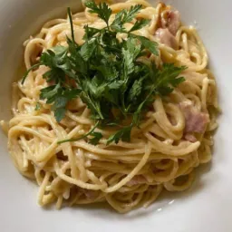 Kremowe spaghetti carbonara z boczkiem i świeżą natką pietruszki w białej, kwadratowej misce, widok z g&oacute;ry.