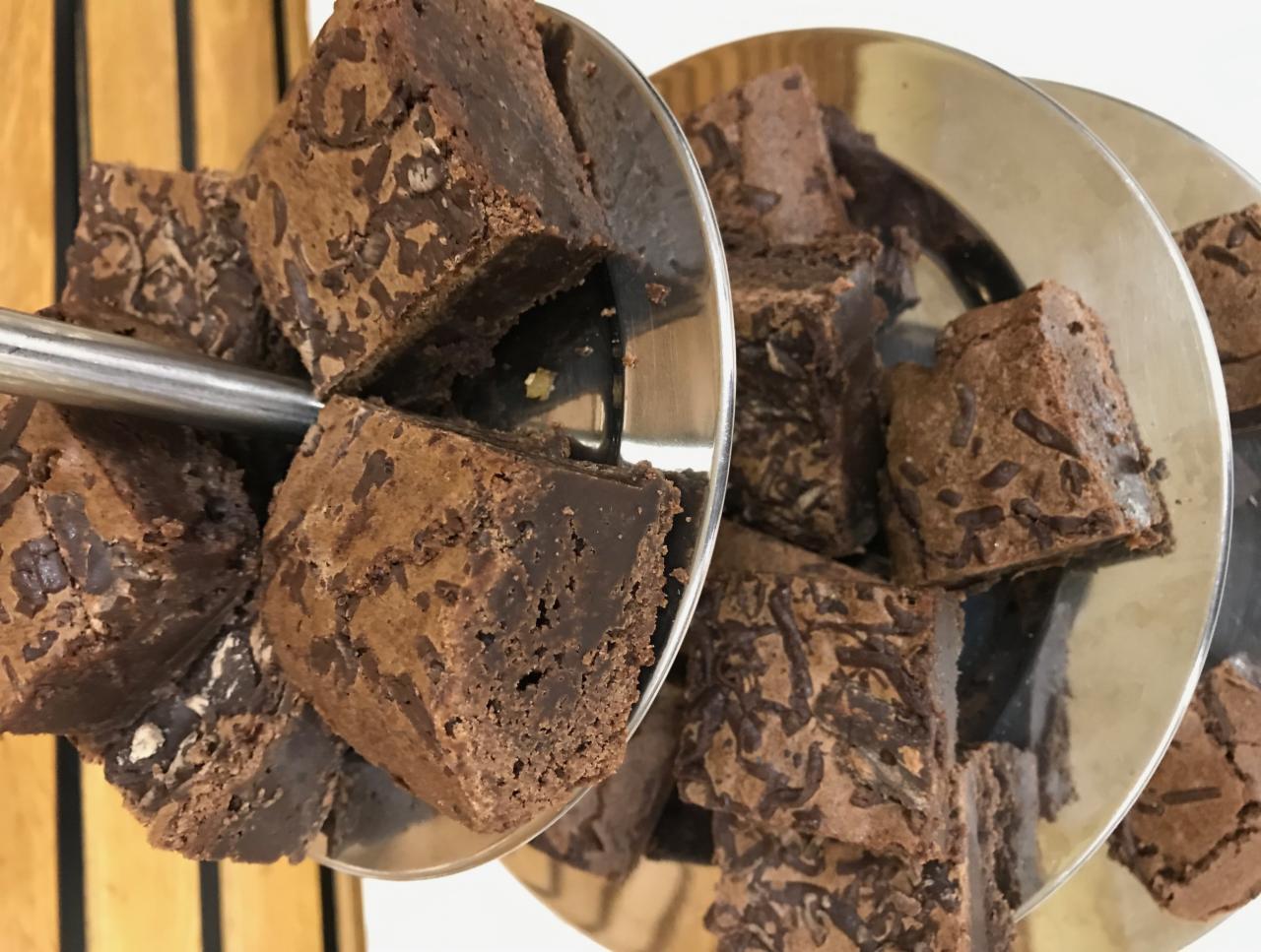 Kwadratowe kawałki czekoladowego ciasta brownie z posypką na srebrnej, trzypoziomowej paterze.