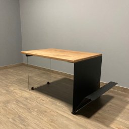 P.H.U. Ja-Ry Jacek Rycharski - Nowoczesny stół z blatem z jasnego drewna, szklanymi nogami i czarną, metalową podstawą z elementem na gazety. Minimalistyczny design, neutralne tło.