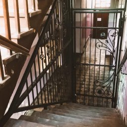 P.H.U. Ja-Ry Jacek Rycharski - Kuta, czarna barierka schodowa z dekoracyjnymi elementami, zabezpieczająca wejście na klatkę schodową. Widok z góry na schody z szarego betonu.