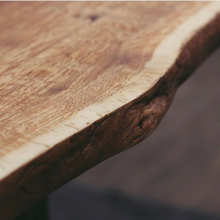 Blat drewniany z naturalną krawędzią, wykończony na gładko, ukazujący unikalny rysunek słojów. Ciepłe oświetlenie podkreśla fakturę drewna.