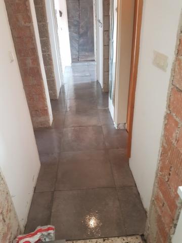 Korytarz w trakcie remontu z nową, ciemną, kwadratową podłogą z płytek; widoczne niedokończone ściany z cegły i białe futryny drzwi.