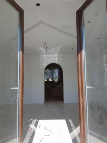 Widok przez otwarte dwuskrzydłowe drzwi balkonowe na wykończone wnętrze z gładkimi, białymi ścianami, łukowatym przejściem i jasną podłogą z płytek. Na podłodze widoczne kable.