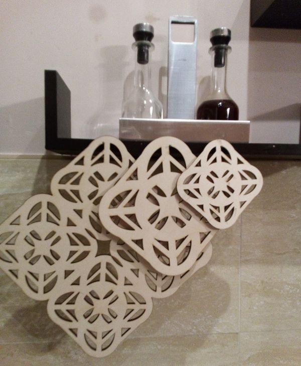 Wycinane laserowo, drewniane podkładki pod naczynia z motywem geometrycznym, ułożone na blacie w pobliżu przypraw w butelkach.