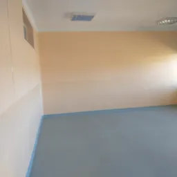 Puste pomieszczenie biurowe z dwukolorowymi ścianami, szarą podłogą i oknem z zieloną roletą.