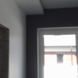 Jpp Painting&Decorating - Pomieszczenie po malowaniu: szara ściana, biały sufit z listwą i okno z widokiem na budynek.