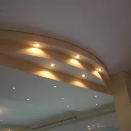 Wykończony fragment sufitu z dekoracyjnym łukiem i wbudowanymi punktowymi oprawami oświetleniowymi emitującymi ciepłe światło.