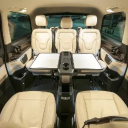 Luksusowe wnętrze busa z beżowymi skórzanymi fotelami, rozkładanym stolikiem i uchwytami na napoje, widok z perspektywy pasażera.