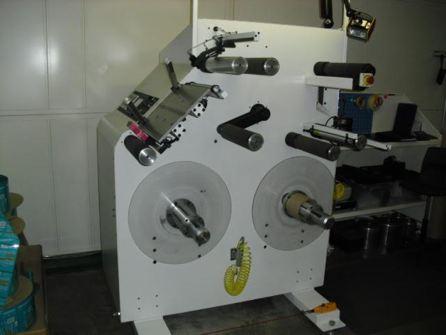 Biała maszyna przemysłowa z dwoma dużymi rolkami i elementami sterującymi, widoczne akcesoria i przewód spiralny.