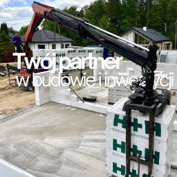 Polbudrol - Generalny Wykonawca - Budowa domu: dźwig podnosi paletę z betonowymi bloczkami komórkowymi H+H na fundamentach. Widoczny pracownik, domy w tle i hasło reklamowe na zdjęciu.
