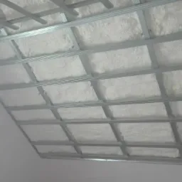 Sufit poddasza z metalową konstrukcją i wypełnieniem z białej piany izolacyjnej, widok z dołu.