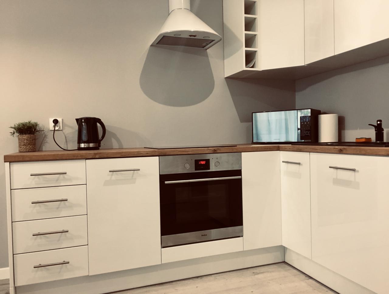 Wnętrze czystej, nowoczesnej kuchni w Szczecinie z białymi szafkami, drewnianym blatem, piekarnikiem Amica i czajnikiem elektrycznym, po profesjonalnym sprzątaniu.