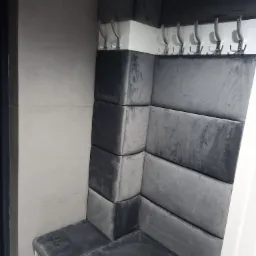 Wnęka z siedziskiem i tapicerowanym panelem ściennym w odcieniach szarości, wykończona wieszakami na ubrania.