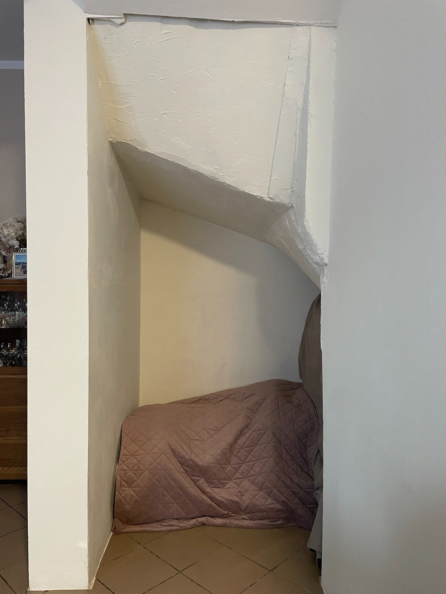 Narożna wnęka w ścianie, zaadaptowana na miejsce do spania z materacem przykrytym pikowaną narzutą w odcieniach różu, pod skośnym stropem.