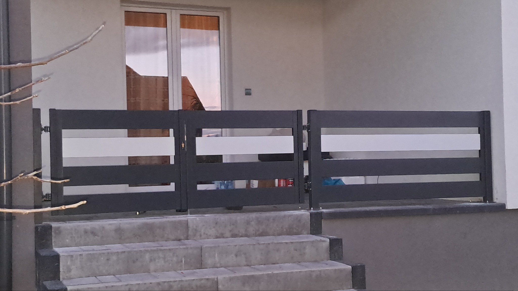 Nowoczesne, grafitowe przęsła z poziomymi białymi wstawkami, zamontowane na schodach wejściowych do domu.